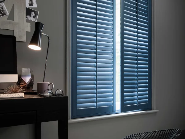 Deep blue plantation shutters closed across a bedroom window in a contemporary interior.