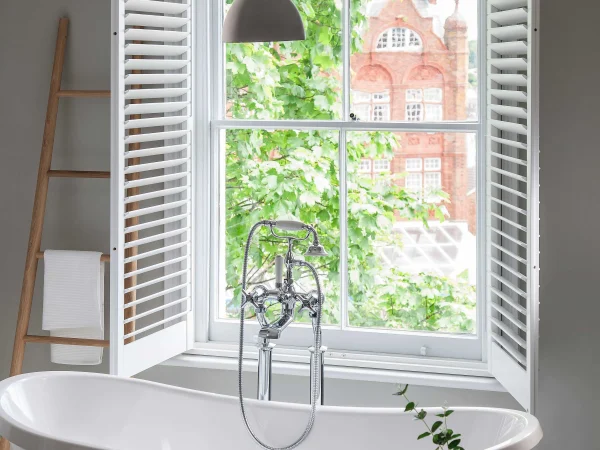 Bluemanor Windows plantation shutter panels opened beside a bathroom window overlooking the garden.