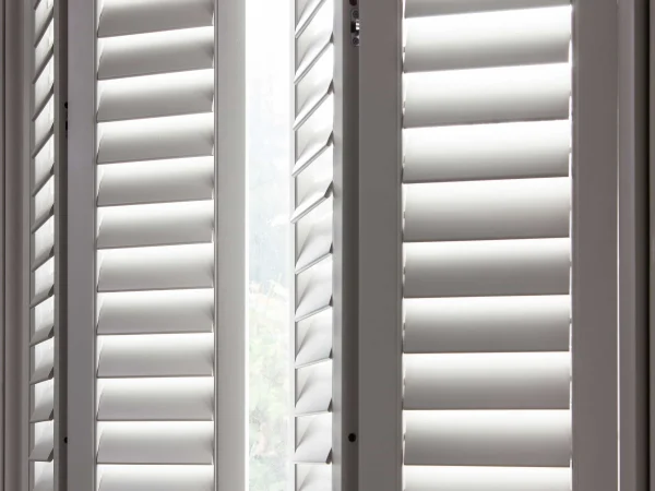 Close-up of open taupe plantation shutter panels and window frame on a bay window.