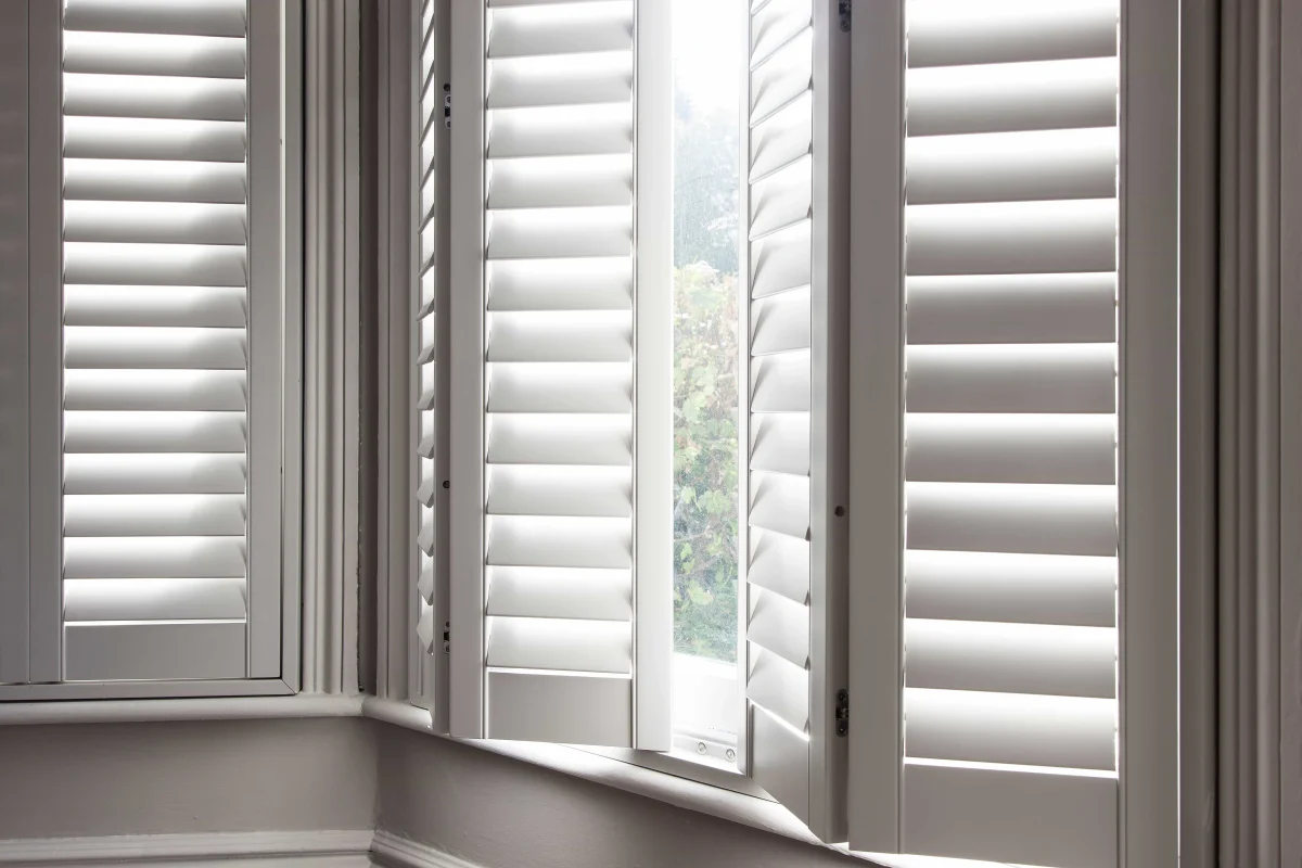 Taupe plantation shutter panels opened on a bay window to reveal the outside view.