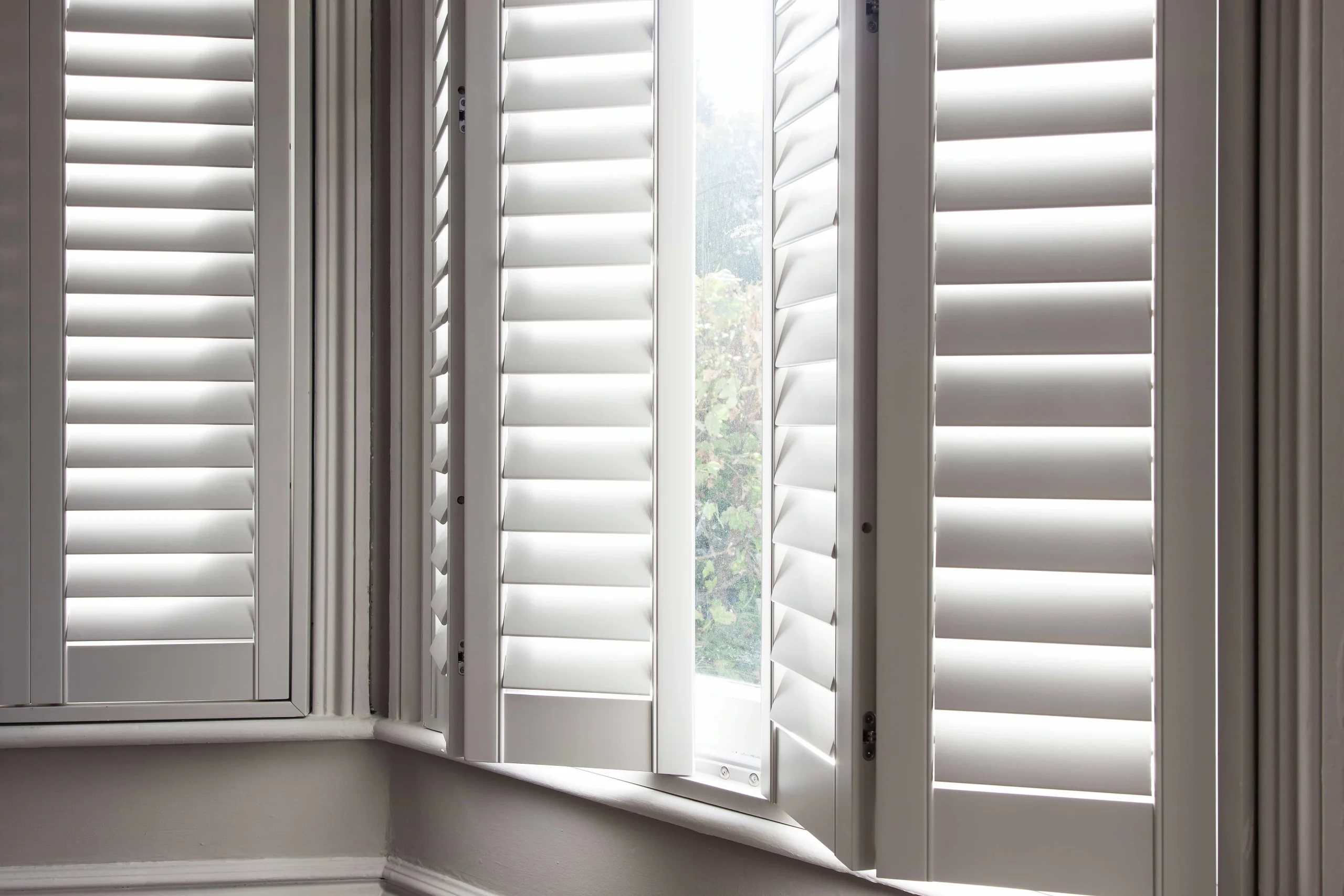 Taupe plantation shutter panels opened on a bay window to reveal the outside view.