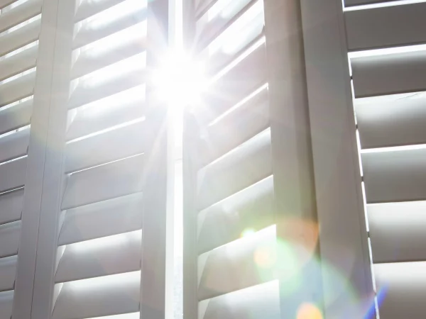 Close-up of sunlight passing through adjustable taupe plantation shutter louvres in a bay window.