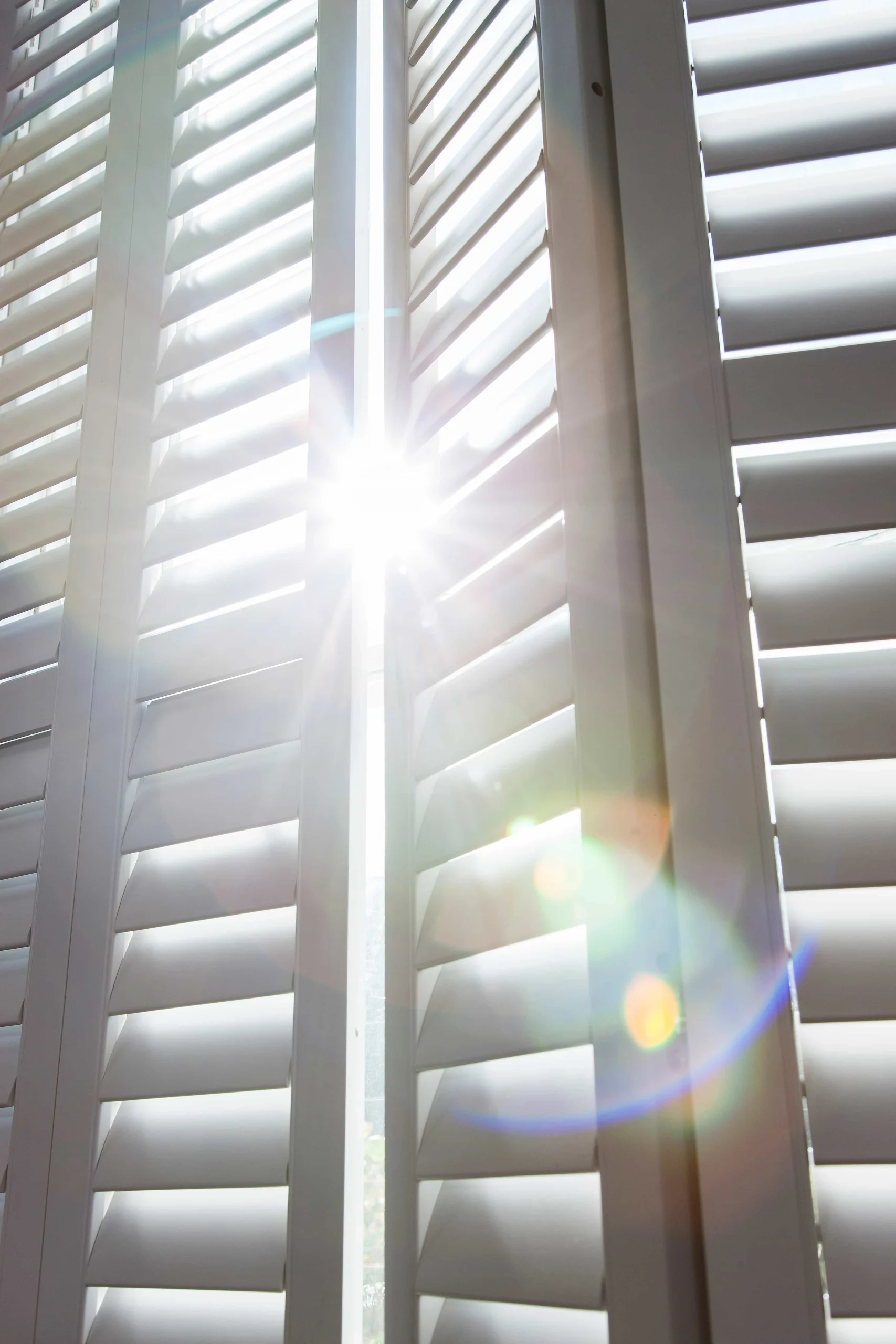Close-up of sunlight passing through adjustable taupe plantation shutter louvres in a bay window.