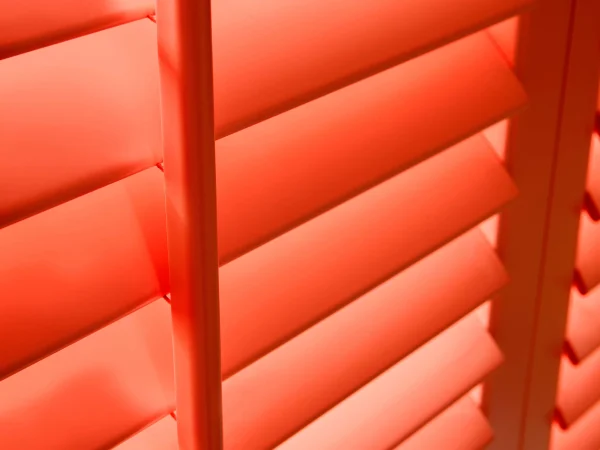 Close-up of bright coral plantation shutter louvres and panel frame.
