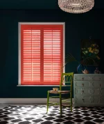 Bright coral plantation shutters fitted in a dark green living room with monochrome flooring.