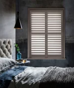 Cockleshell plantation shutters fitted to a bedroom window, providing elegant light control, privacy and a warm neutral finish.