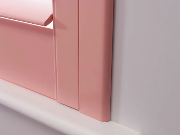 Close-up of a coral blush plantation shutter frame and louvres fitted neatly within a white window reveal.