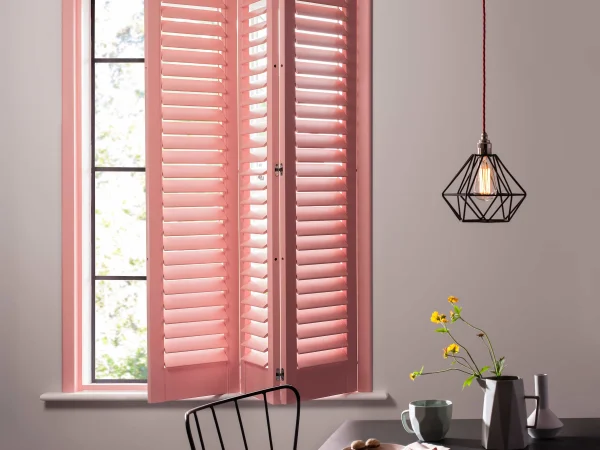 Coral blush plantation shutter panels opened to reveal the window in a modern dining room.