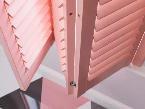 Close-up of an open coral blush plantation shutter panel showing adjustable louvres and contemporary coloured finish.