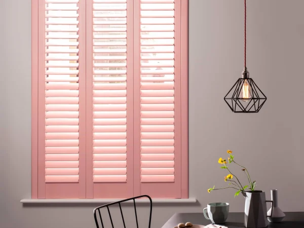 Coral blush plantation shutters closed across a window in a modern dining space.