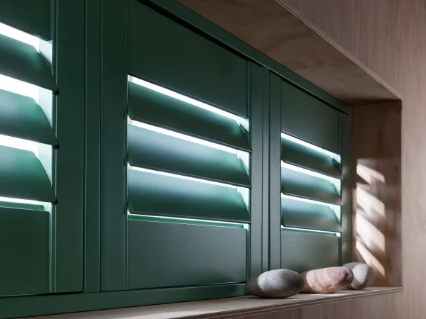 Dark green plantation shutters fitted within a deep window reveal above a built-in seat.
