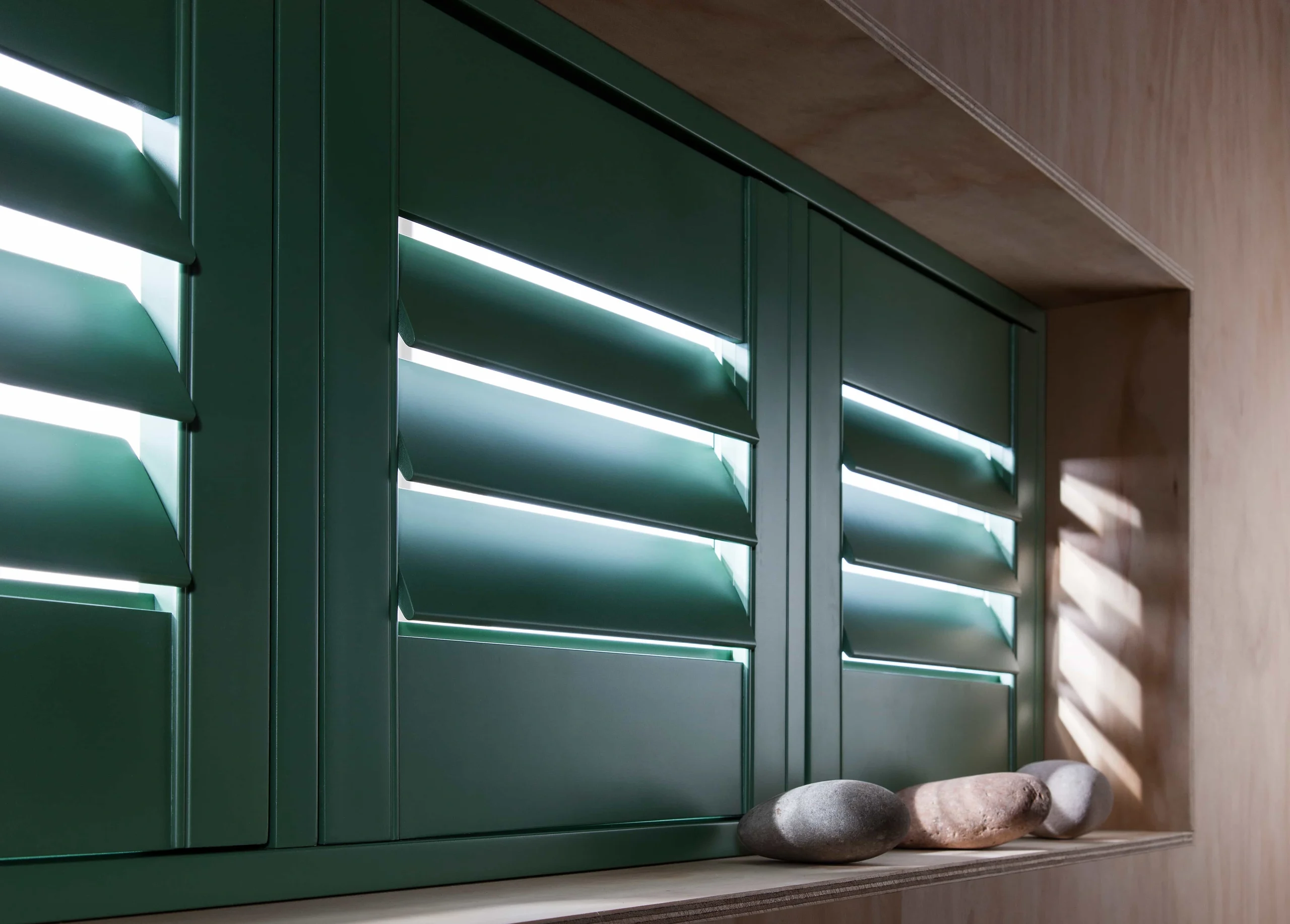 Dark green plantation shutters fitted within a deep window reveal above a built-in seat.