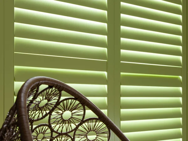 Lime green plantation shutters behind a decorative woven chair in a contemporary room.