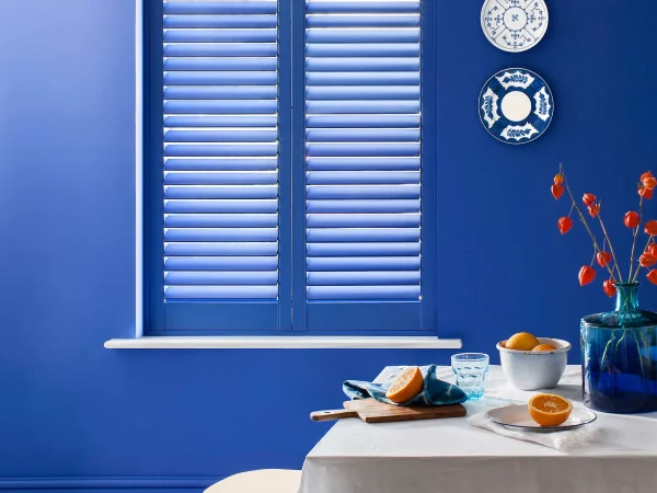 Lindos blue plantation shutters fitted to a dining room window with matching blue walls.