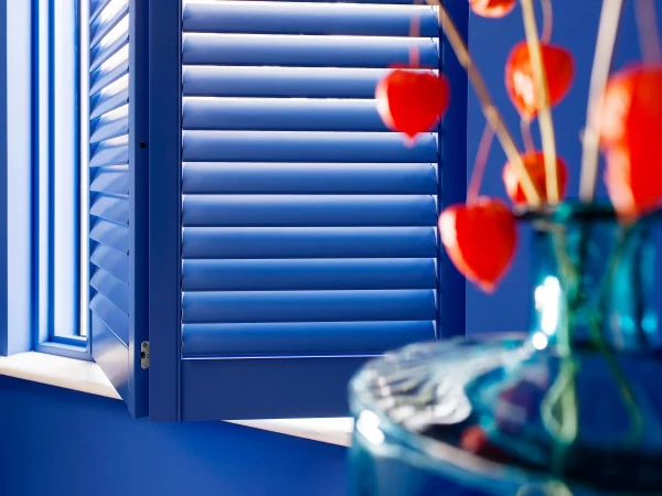 Lindos blue plantation shutters opened beside a window with colourful flowers in the foreground.