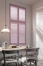Pastel pink full-height plantation shutters fitted to a tall dining room window.