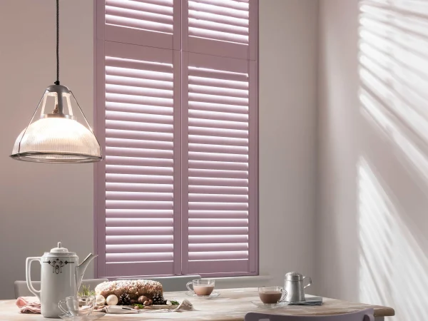 Pastel pink full-height plantation shutters fitted to a tall dining room window.