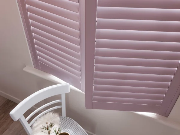 Pastel pink plantation shutter panel opened above a small white table.
