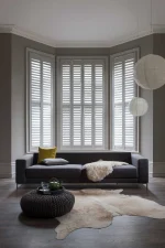 Taupe plantation shutters fitted across a large bay window in a contemporary living room.