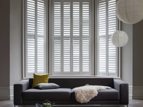 Taupe plantation shutters fitted across a large bay window in a contemporary living room.
