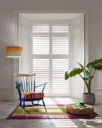 White plantation shutters fitted to a shallow bay window in a modern living area.