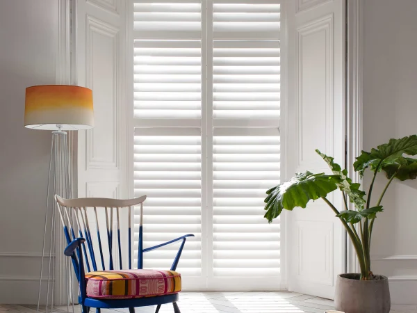 White plantation shutters fitted to a shallow bay window in a modern living area.