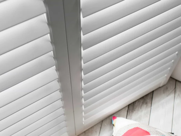 Close-up of white plantation shutter panels fitted neatly above a light wood floor.