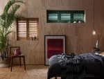 A bedroom featuring natural wood-grain shutters and contrasting dark green plantation shutters.