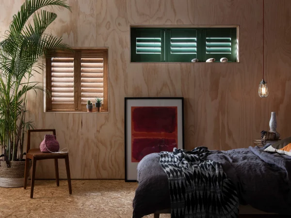 A bedroom featuring natural wood-grain shutters and contrasting dark green plantation shutters.