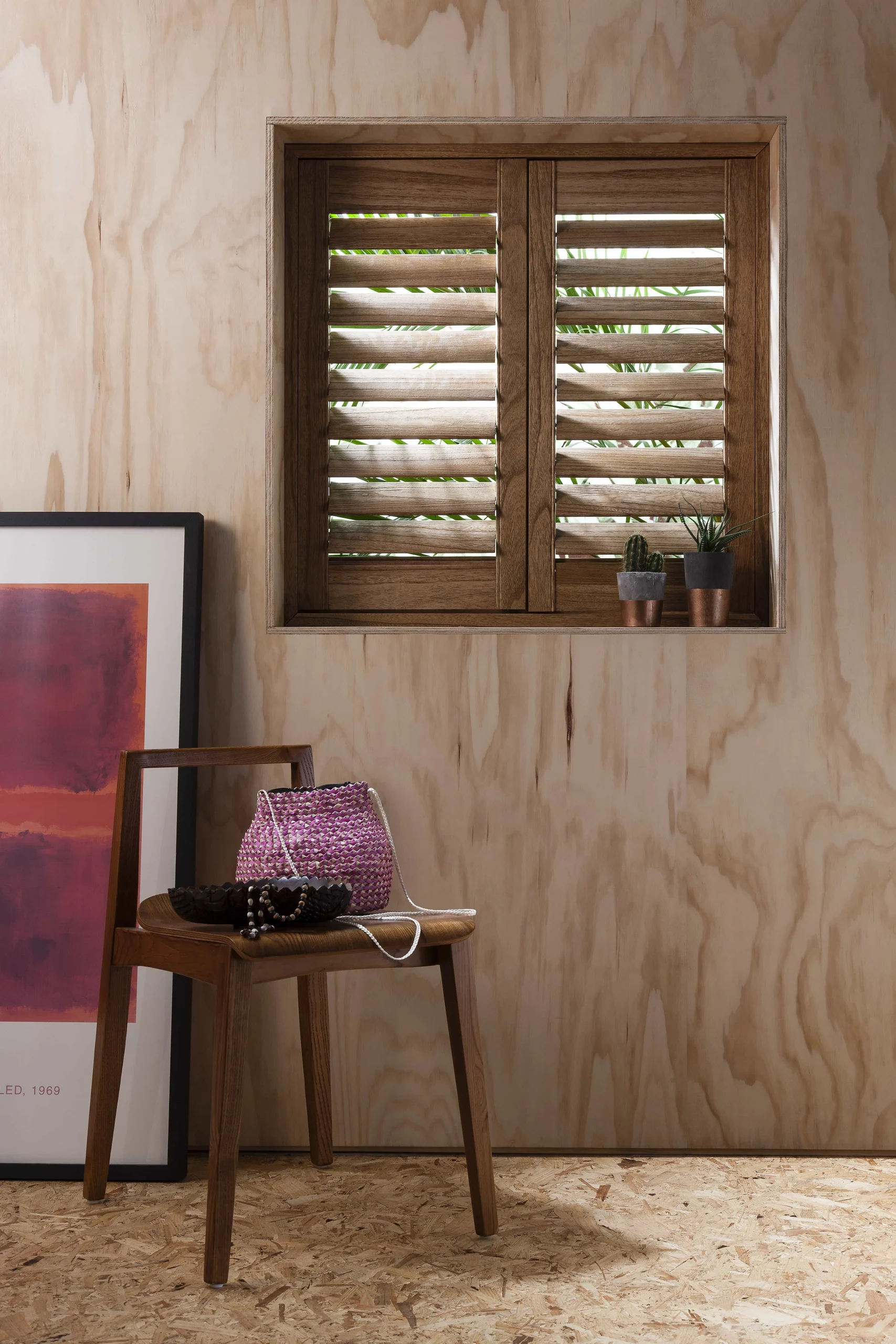 Wood-grain plantation shutters fitted to a small window in a natural plywood-lined room.